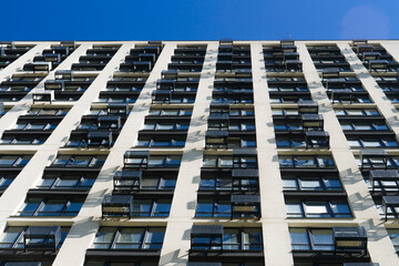 Abstract low-angle view of a modern high-rise residential building facade with repetitive rows of windows and white walls under a clear blue sky