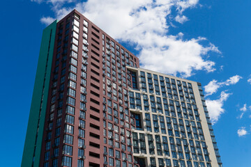 Striking architectural detail of a contemporary high-rise apartment building with contrasting colored facades set against a dramatic, cloudy blue sky