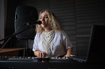 Caucasian woman singing into microphone and playing synthesizer. 
