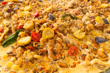 Full-frame close-up of a rich, creamy paella dish filled with mussels, shrimp, corn, and cherry tomatoes, cooked in a rich yellow sauce