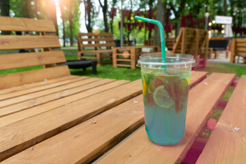 Close-up of a refreshing blue citrus and mint lemonade cocktail on a rustic wooden pallet table in a sunny summer outdoor park cafe