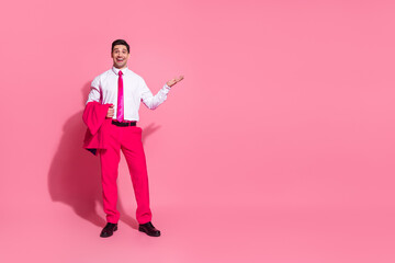 Obraz premium Confident young man in bright pink suit and tie posing with charisma against a vibrant pink studio background