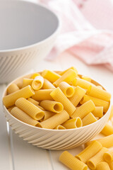 Uncooked rigatoni pasta in bowl on white table.