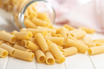 Uncooked rigatoni pasta on white table.