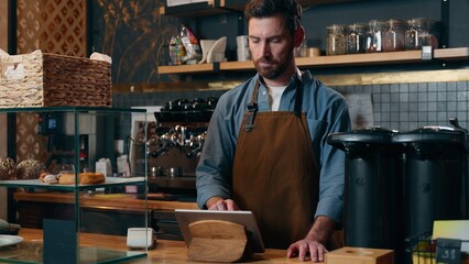 Serious Caucasian barista bartender male owner typing tablet in cafeteria catering job man manager purchase food online shop restaurant worker waiter guy swiping screen gadget tech cafe small business