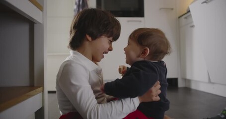 Older brother sitting on the kitchen floor embracing his baby sibling, sharing laughter and affection, showing warmth, trust, and the joyful emotional bond of family love at home - Powered by Adobe