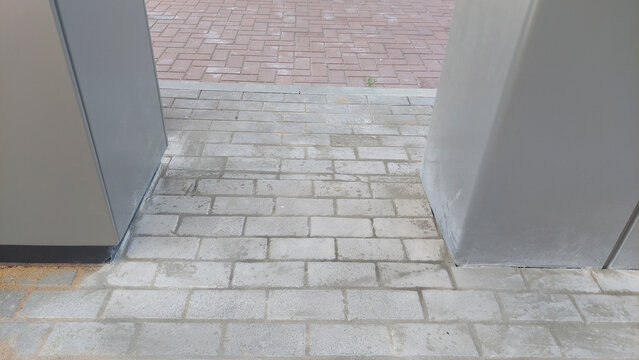 Fototapeta Paved walkway between two gray structures near a brick surface in a sunny outdoor area