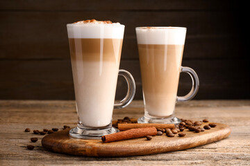 Tasty latte macchiato in glass cups, coffee beans and cinnamon on wooden table, closeup