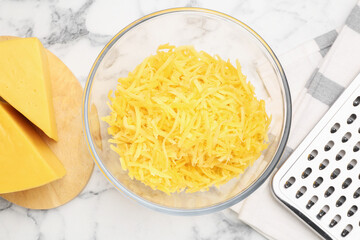 Grated cheese in bowl, fresh pieces and grater on white marble table, flat lay