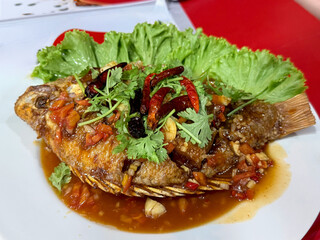 Thai-style deep fried fish with spicy chili sauce and herbs, served with lettuce. Traditional Asian seafood dish.