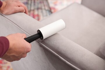 Man cleaning sofa with lint roller at home, closeup