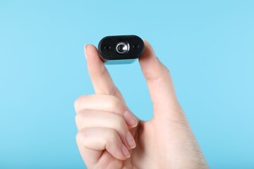 Woman with hidden spy camera on light blue background, closeup