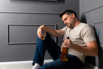 Man sitting on the floor with alcohol in a dim room, showing signs of being drunk