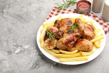 Grilled chicken drumsticks served with french fries and spices on grey table, closeup. Space for text