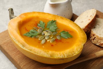 Tasty pumpkin cream soup with seeds, parsley and bread on grey textured table, closeup