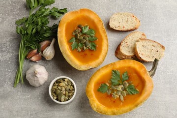 Tasty pumpkin cream soup with seeds, parsley, garlic and bread on grey textured table, flat lay
