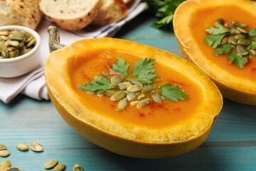 Tasty pumpkin cream soup with seeds and parsley on light blue wooden table, closeup