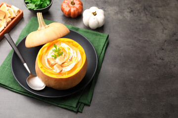 Tasty pumpkin cream soup with croutons and parsley served in pumpkin on grey table, space for text