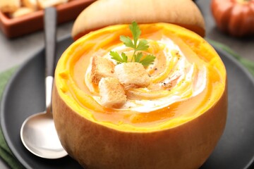 Tasty pumpkin cream soup with croutons and parsley served in pumpkin on table, closeup