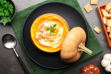 Tasty pumpkin cream soup with croutons and parsley served in pumpkin on grey table, flat lay