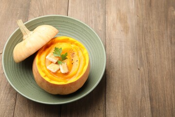 Tasty pumpkin cream soup with parsley and croutons served in pumpkin on wooden table, closeup. Space for text
