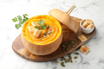 Tasty pumpkin cream soup with seeds, parsley and croutons served in pumpkin on white marble table, closeup