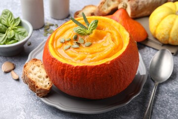 Tasty pumpkin cream soup with seeds and basil served in pumpkin on grey table, closeup