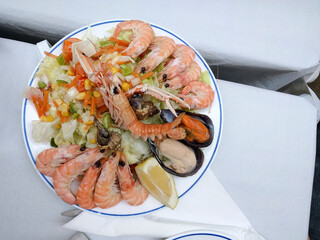 A vibrant plate of fresh seafood, featuring shrimp, langoustine, and mussels, is served with a crisp green salad and a lemon wedge.