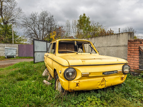 Vinnytsia, Ukraine - October 23, 2025: Front view of an old yellow ZAZ-968M car discarded in a suburban yard with autumn trees and cloudy sky.