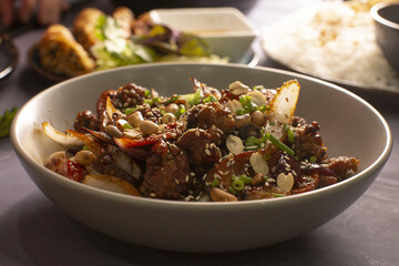 A tasty bowl of stirfried meat and colorful veggies, garnished with roasted peanuts and fresh herbs