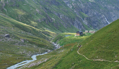 Summer landscape with refuge Mario Bezzi in Gran Paradiso national Park in Italy. Destination for climbers and mountain lovers. Dense green vegetation all around. A group of hikers going to the refuge