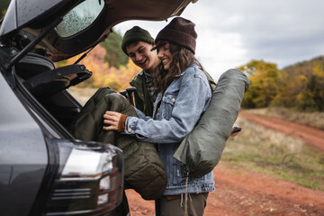 Young couple packing camping gear in car trunk for road trip