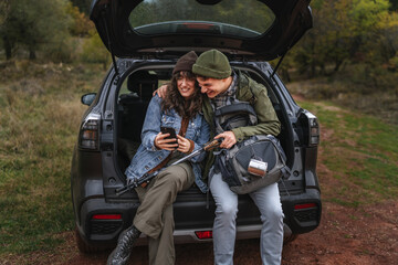 Happy couple relaxing on car trunk during hiking trip