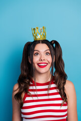 Cheerful young woman with ponytails and golden crown against blue backdrop exuding charm and...