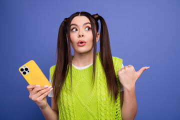 Young woman with bright lime green sweater holds yellow smartphone and looks surprised and playful...