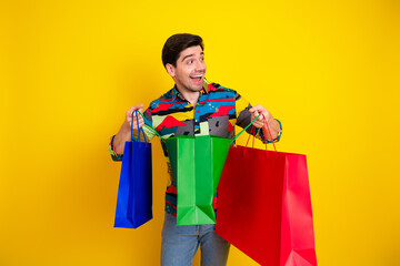 Young man with colorful shirt carries multiple shopping bags against a bright yellow background...