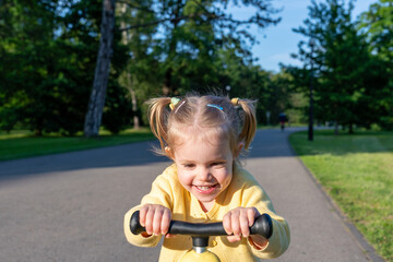 Scooter child. Girl riding scooter toddler. Yellow outdoor activity park road.
