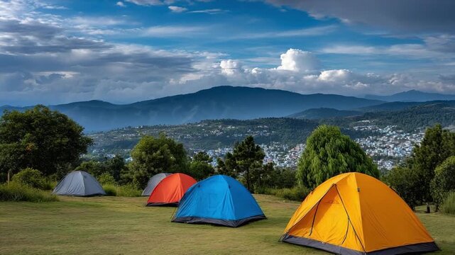 Colorful tents pitched on a grassy field with distant mountains and a town in the background.