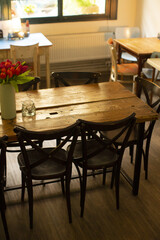 Cafe table scene, Sunlit cafe with floral decor, Wooden table setup with tulips and chairs, Inviting brunch scene with natural grain table and fresh flowers
