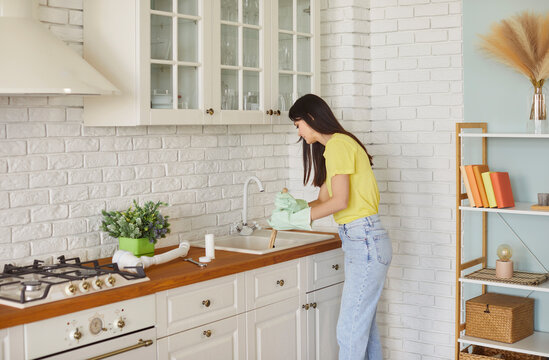 Young woman wearing rubber cleaning gloves standing in kitchen while holding plunger and unclogging blocked sink drain, experiencing household problems, solving issue. Household chores concept