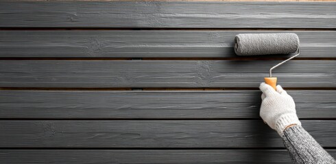 hand in gray gloves paints the brown wooden planks