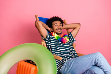 Young mixed race man relaxing in a striped shirt with a colorful lei on pink background lounging in chair for lifestyle fashion and leisure promotion