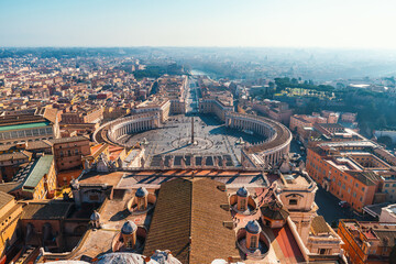 Aerial view of St. Peter's Square in Vatican City with colonnades and ancient obelisk and Rome skyline in background on sunny day. Italian architecture. Travel landmark in Rome city, Italy