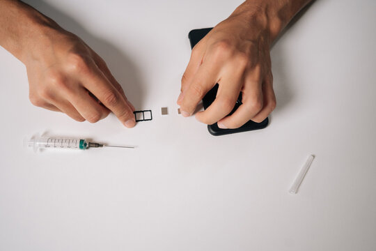 Skilled technician male removing smartphone sim card with precision ejector tool, medical needle nearby highlighting technical proficiency against clean white surface. Concept of modern communication