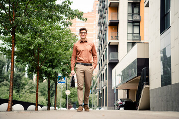 Young businessman in formal attire walking confidently in a modern urban street surrounded by trees...