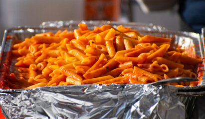Penne pasta in a tin foil tray outside 