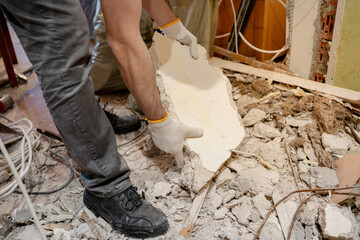 Close-up of a laborer using manual effort to lift a heavy piece of construction debris,...