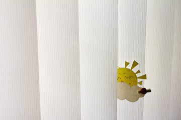 a child's drawing of a sun on a clothespin and white blinds