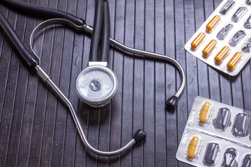 stethoscope and pills on a black wooden surface