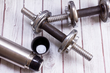 two dumbbells and a thermos for water on a wooden surface